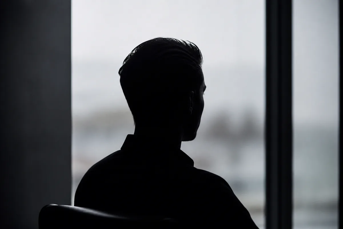 Profil d’homme aux cheveux courts coiffés vers l’arrière en contre-jour devant une fenêtre de salon