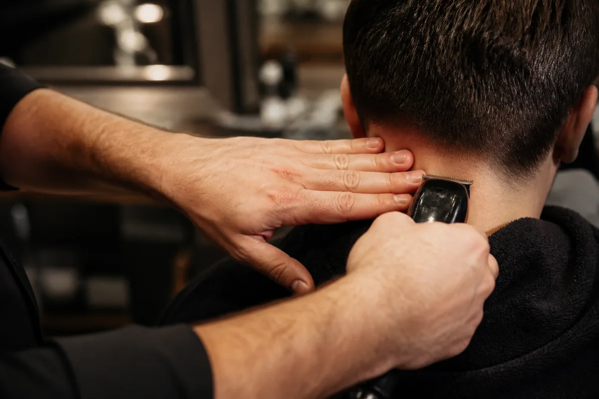 Mains d’un coiffeur travaillant la ligne de nuque d’un client à la tondeuse dans un salon
